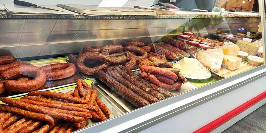 Kühltheke mit Wurstringen, Mettenden, Aufschnitt und Käselaiben.