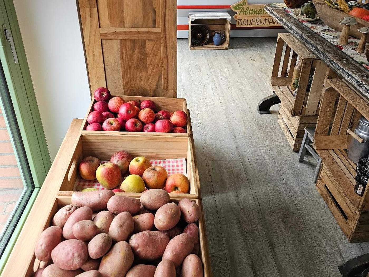 Eine Holzkiste mit roten Kartoffeln, darüber Äpfel in einer Steige.