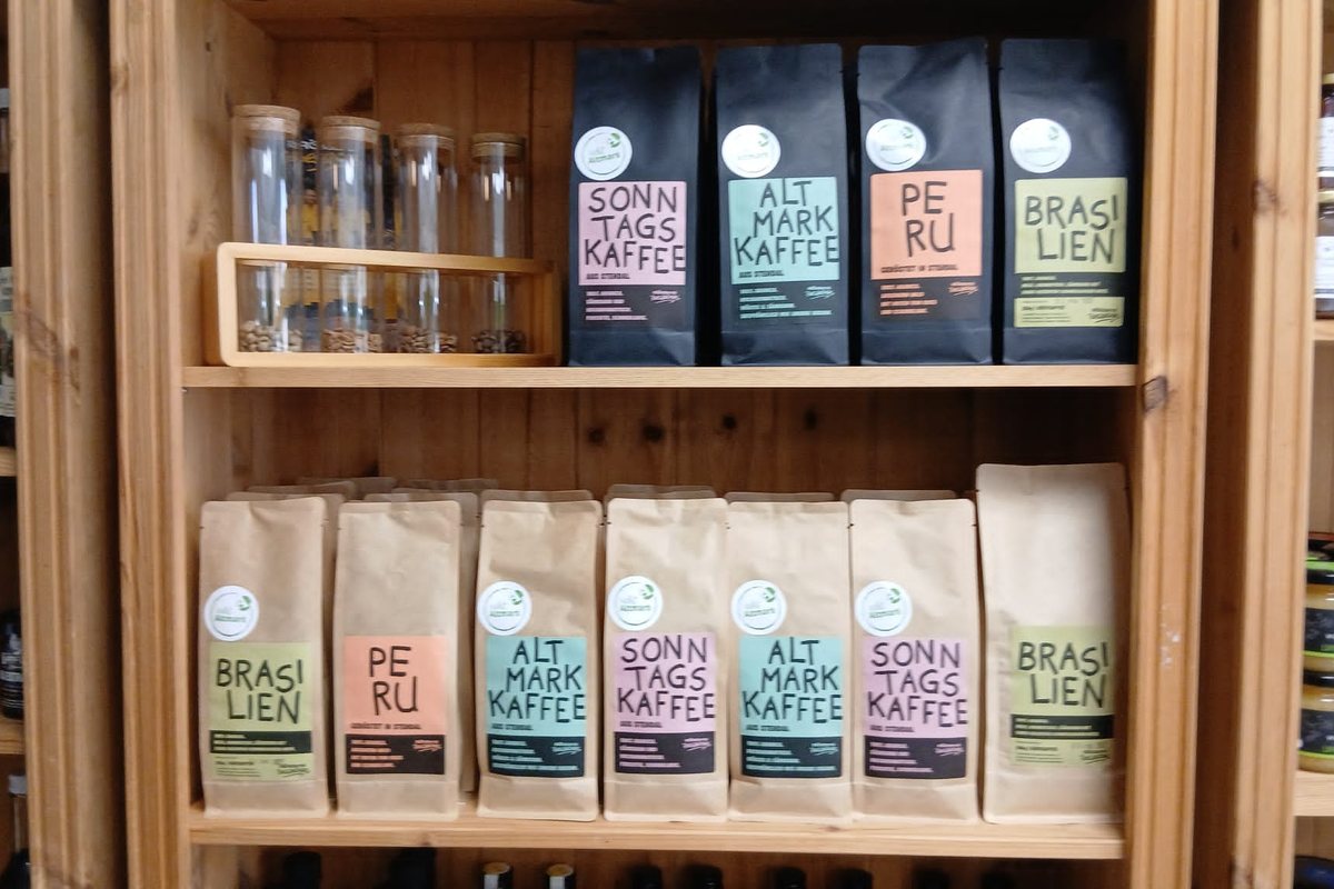 Kaffeebeutel im Holzregal mit den Sorten Sonntagskaffee, Altmark Kaffee, Peru und Brasilien, daneben Gläser mit Kaffeebohnen.