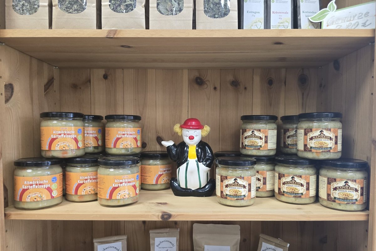 Ein Regal mit Gläsern Altmärkische Kartoffelsuppe und Napoleon Rissolée-Suppe, in der Mitte eine Clownsfigur aus Keramik.