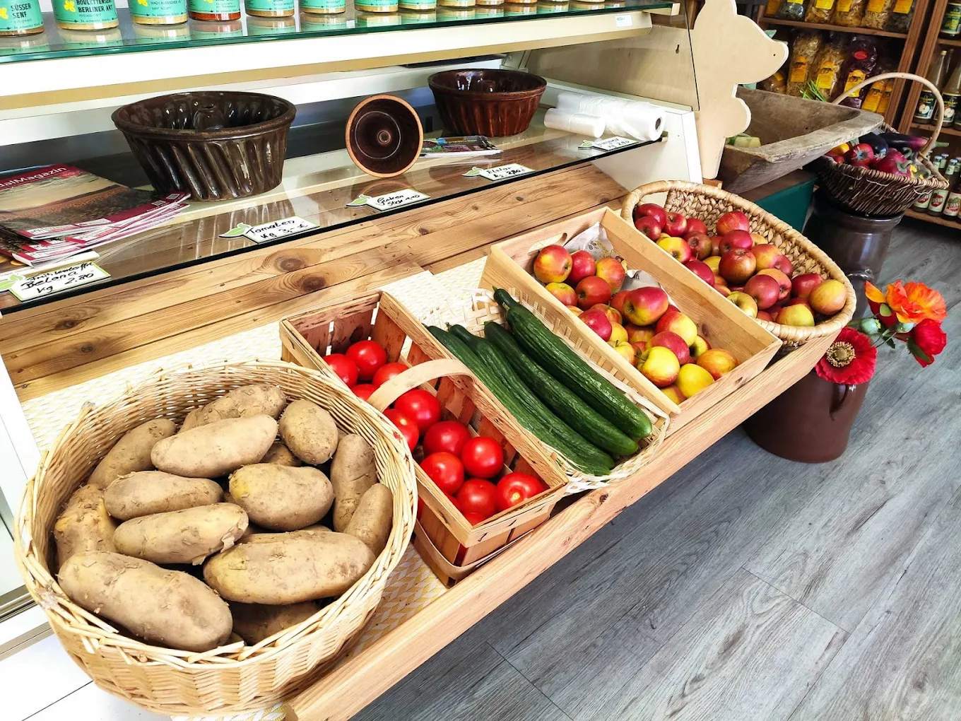 Verkaufstisch mit Kartoffeln, Tomaten, Salatgurken und Äpfeln in Körben und Holzsteigen.